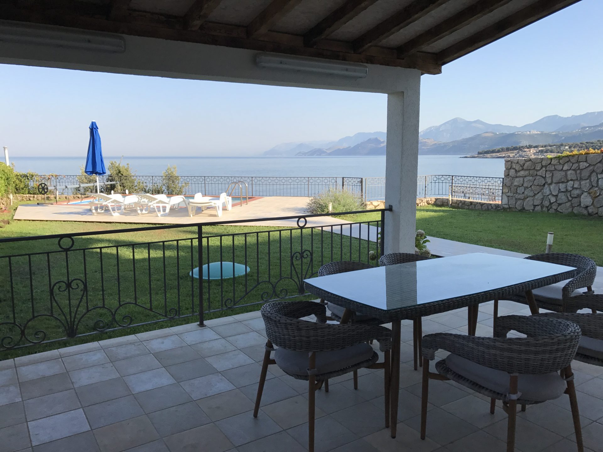 Villa terrace in Utjeha, Montenegro: wicker furniture, sea view, pool and mountains, tiled flooring and lawn.