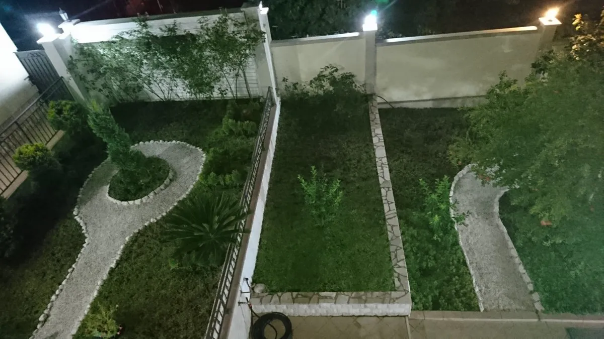 Night view of a enclosed garden with lawns, gravel paths, and an illuminated perimeter wall.