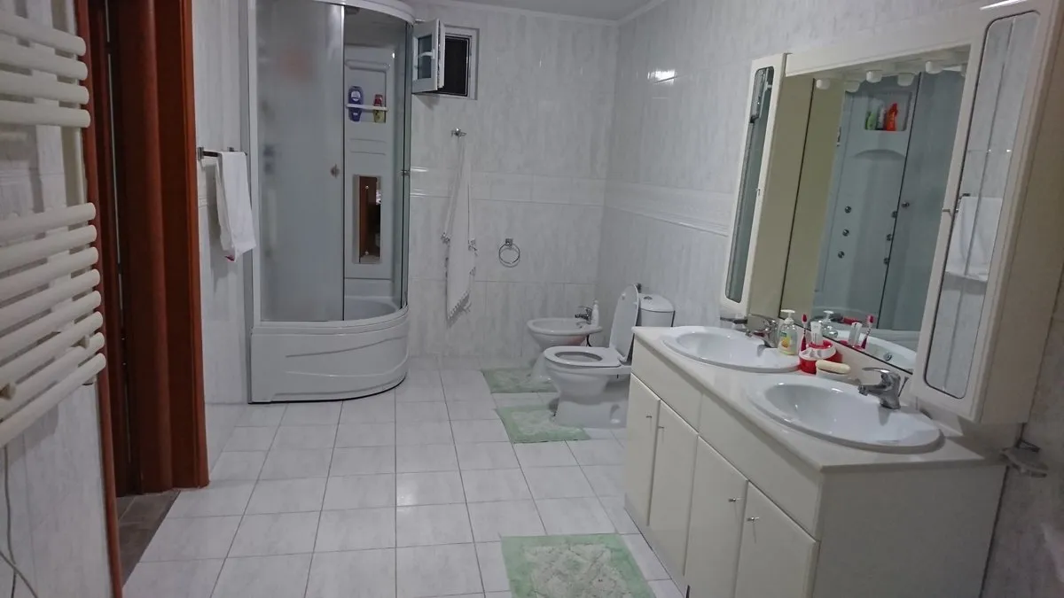 Bathroom featuring a shower stall, toilet, bidet, and double sink vanity unit.