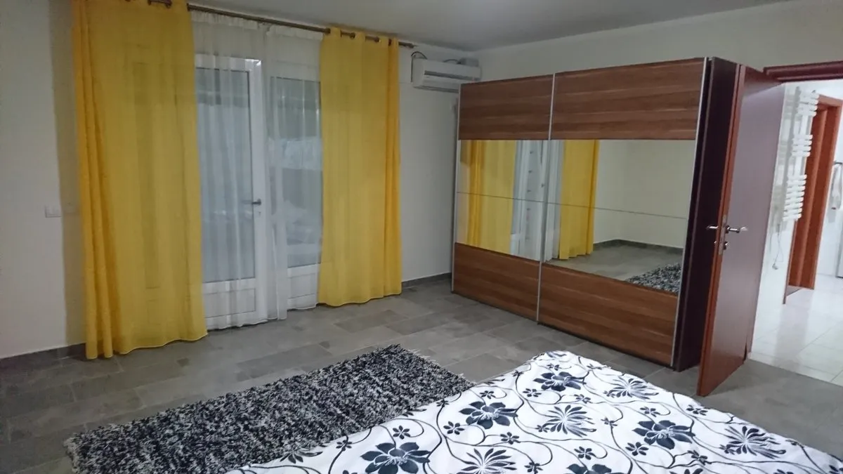 Bedroom with floral bedding, large mirrored wardrobe, yellow curtains, and gray tiled floor.