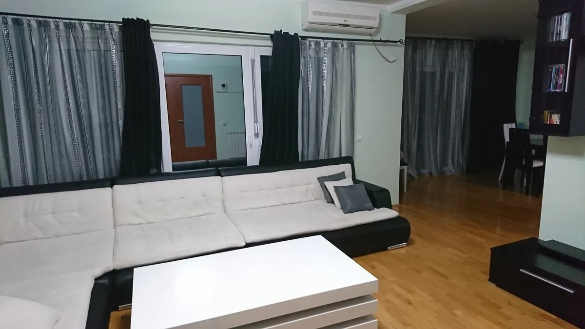 Living room with a large L-shaped sofa, white coffee table, and wooden flooring.
