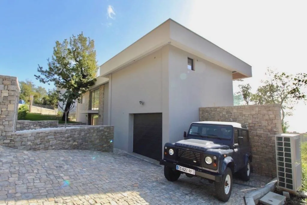 Exterior view of a modern house with a garage, stone wall, and a parked Land Rover on a cobblestone driveway.