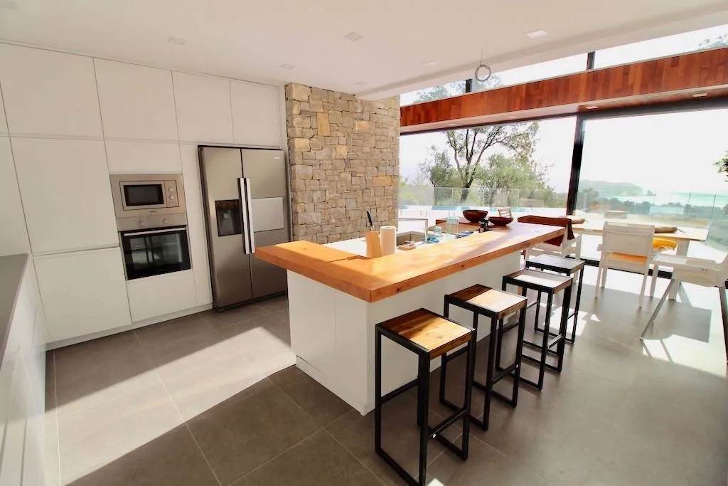 Modern kitchen with white cabinets, wooden island countertop, stainless steel fridge, and built-in appliances.