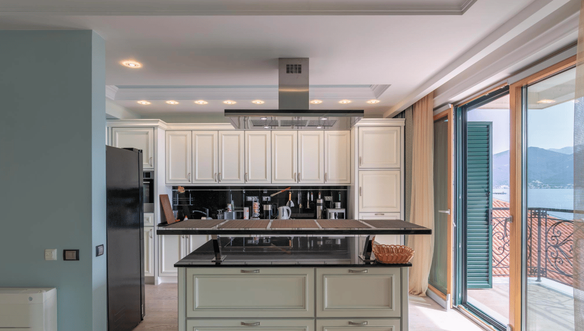 Modern kitchen with island and sea view in a villa, Bijela, Montenegro: light-colored cabinetry, black backsplash, and appliances.