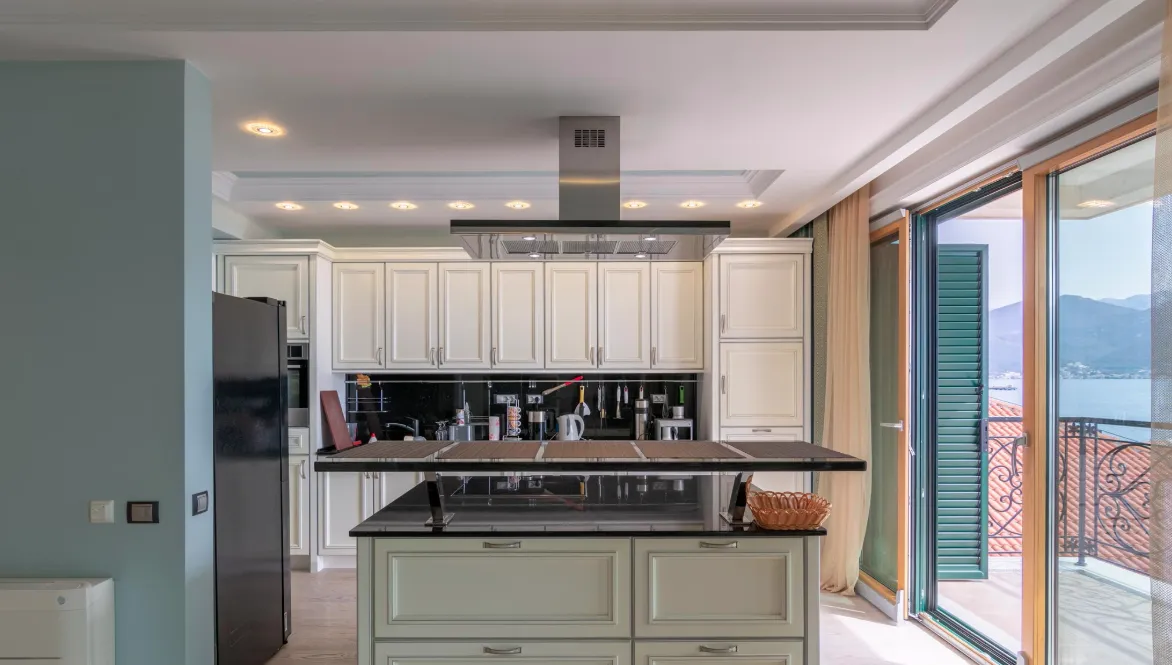 Modern kitchen with island, white cabinets, black countertop, stainless steel hood, and balcony access.