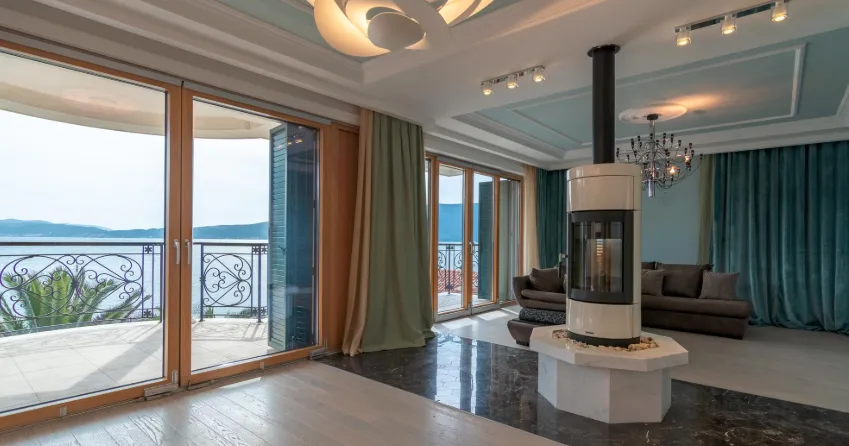 Living room with a brown sofa, central freestanding fireplace, and large glass doors opening to a balcony.