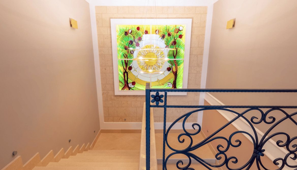 Staircase with wrought-iron railings and a stained-glass window in a luxury villa in Bijela, Montenegro. Interior with stone finishes.