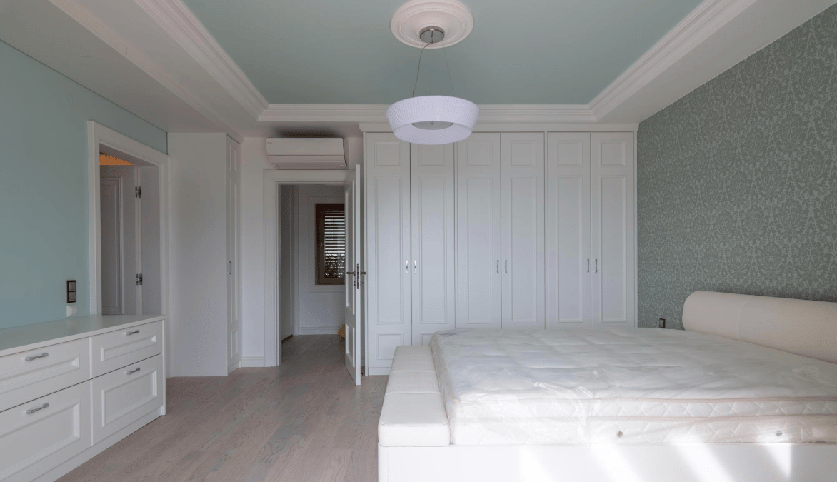 Bright bedroom with white furniture, built-in wardrobe, and bed in a villa in Bijela, Montenegro. Modern interior.