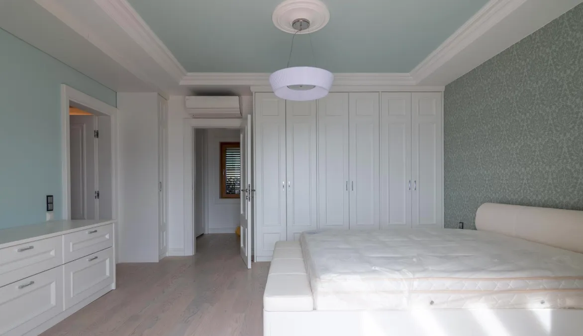 Bright bedroom with a white bed, built-in wardrobe, and light blue walls.