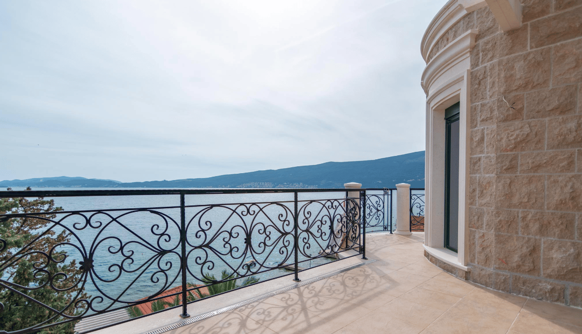 Spacious terrace of a villa in Bijela, Montenegro, with wrought-iron railing and panoramic views of the sea and mountains.