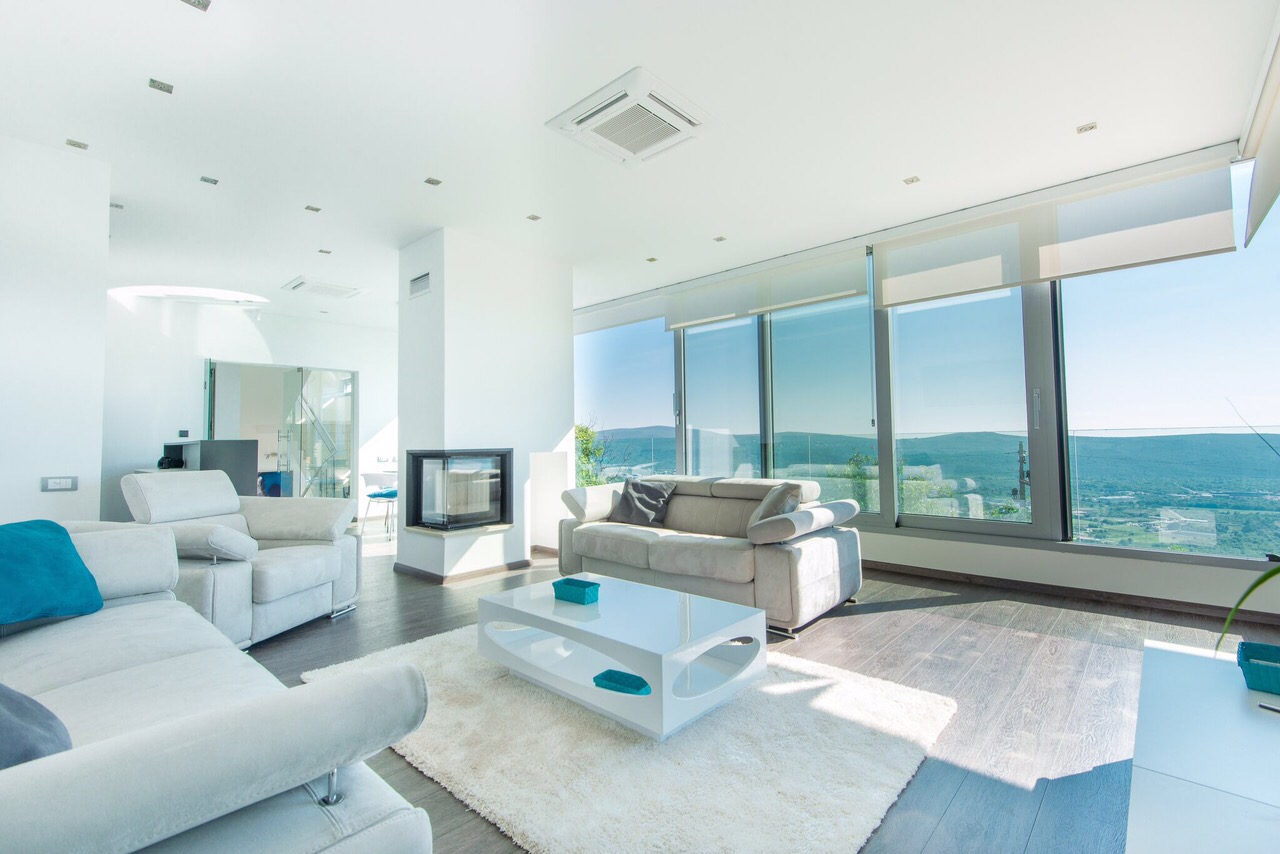 Modern living room with panoramic windows and mountain views in a villa in Kotor, Montenegro: light furniture and a fireplace.