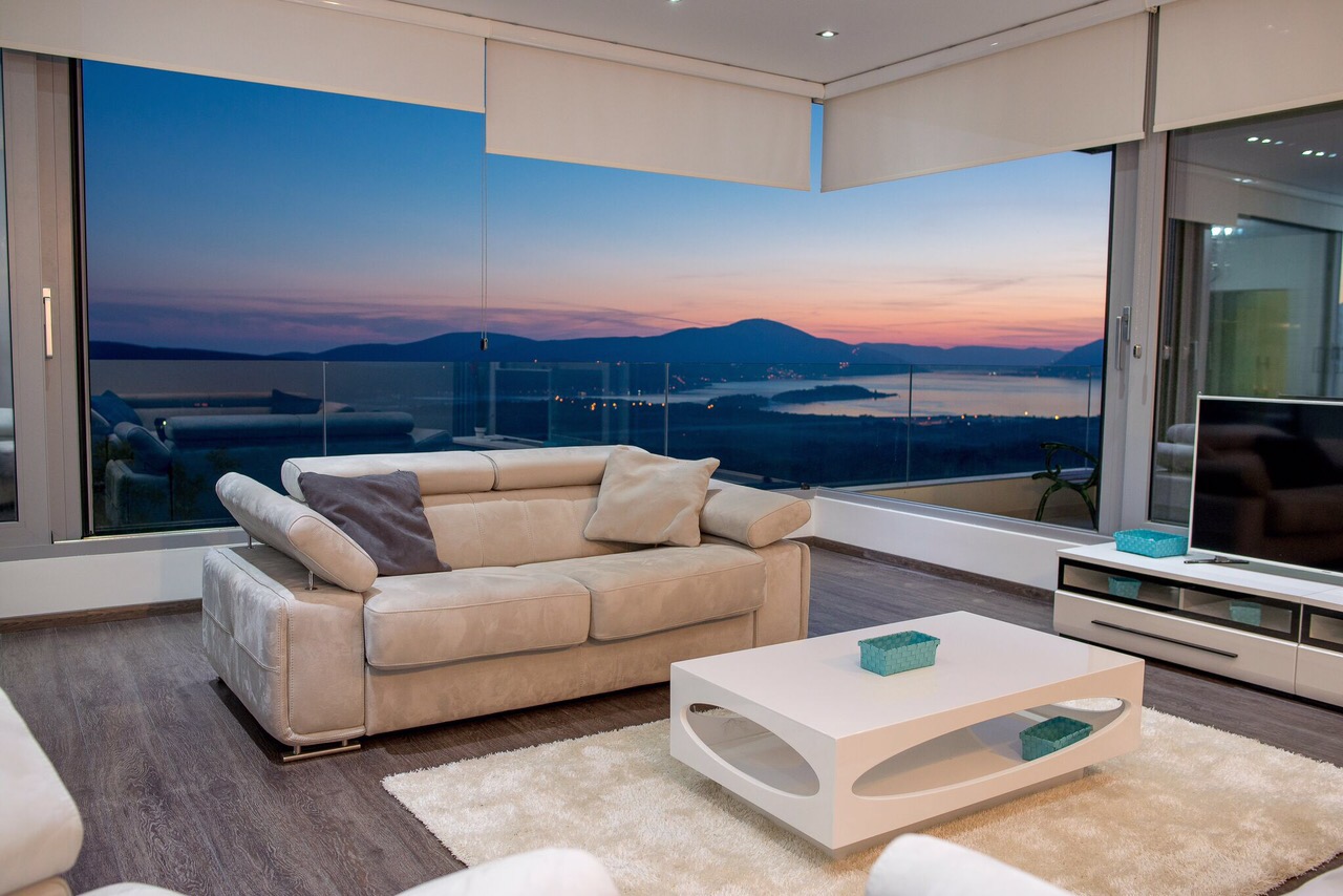 Villa living room in Kotor, Montenegro: panoramic windows with sea and mountain views, a light-colored sofa, and a modern interior.