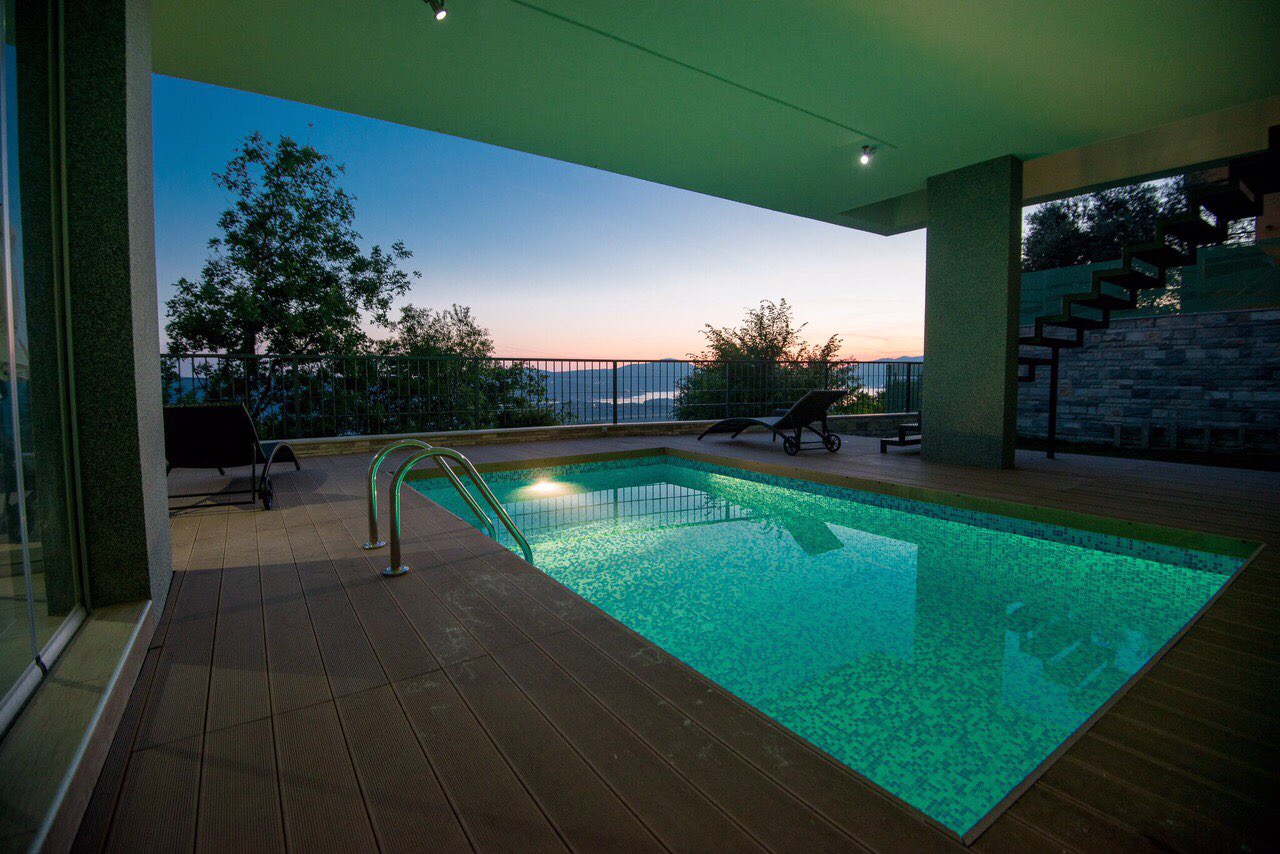 Open-air swimming pool with lighting and a terrace at a villa in Kotor, Montenegro, with panoramic views of the mountains and sunset.