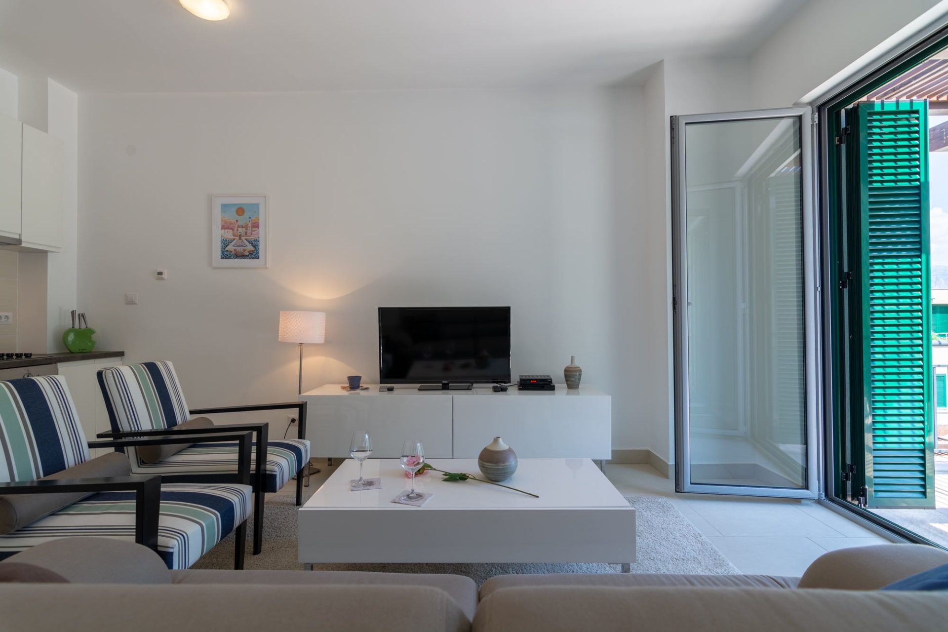 Bright living room in an apartment in Morinj, Montenegro: white furniture, striped armchairs, and access to a terrace with blinds.