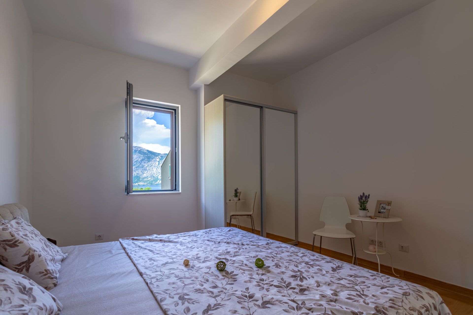 Bedroom in an apartment in Morinj, Montenegro: a double bed, mirrored wardrobe, and a view of the mountains and the sea from the window.