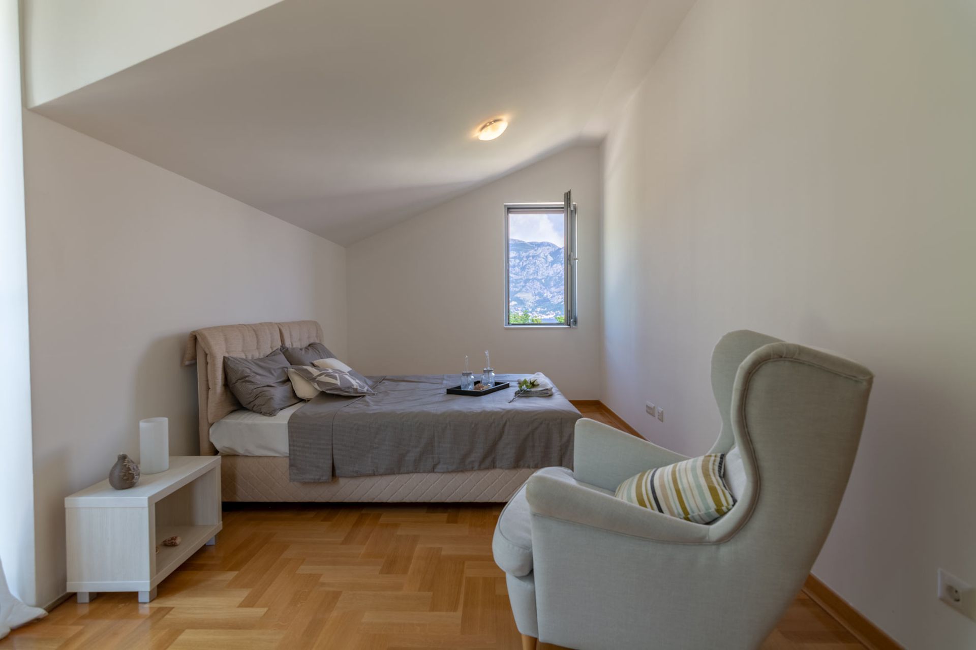 Cozy bedroom in an apartment in Morinj, Montenegro: a double bed, an armchair, and a mountain view from the attic window.