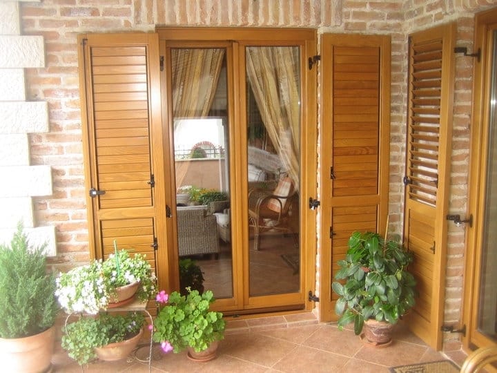 Villa balcony in Orahovac, Montenegro: brickwork, wooden shutters, terracotta tiles, and houseplants.