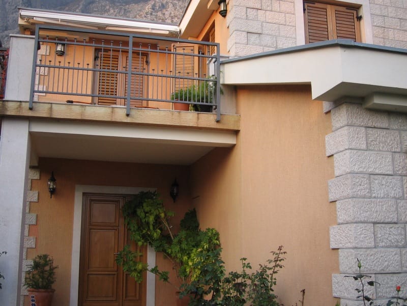 Villa facade in Orahovac, Montenegro: stone cladding, a cozy balcony with wrought-iron railing, and wooden shutters.