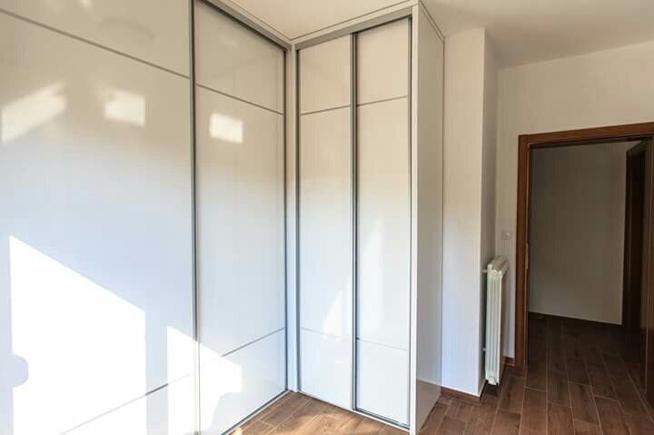 Built-in white glossy sliding wardrobe in the bedroom of a house in Šušanj, Montenegro, with wood-look flooring.