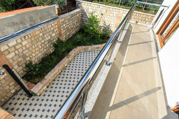 Balcony with tiled flooring and metal railing in a house in Shushan, Montenegro, overlooking a private courtyard with a garden.