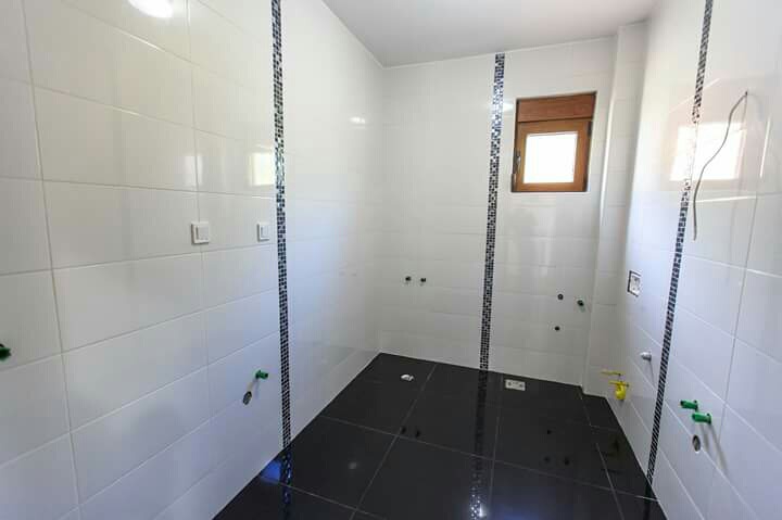 Bathroom with tiled finish in an under-construction building in Shushan, Montenegro: white walls and a black floor with mosaic.