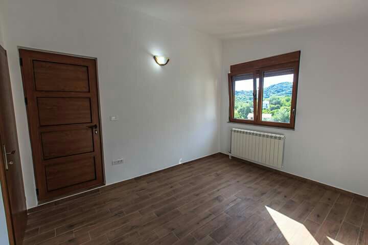 Bright bedroom in a house in Shushan, Montenegro: wooden doors, wood-look flooring, radiator, and a view of green mountains.