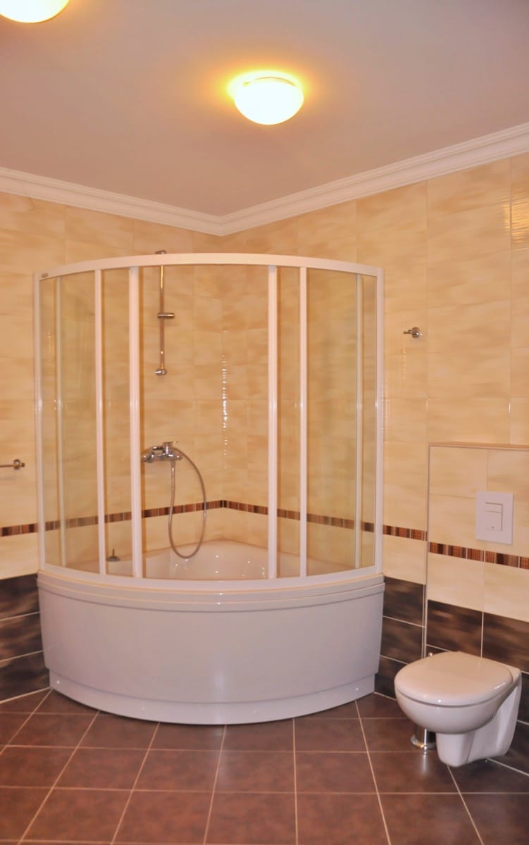 Bathroom featuring a corner shower enclosure with glass panels and a wall-mounted toilet against beige tiles.