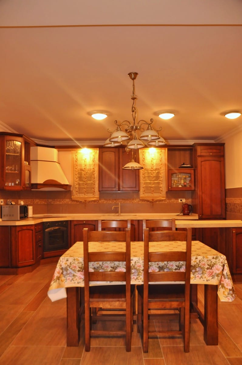 Kitchen with wooden cabinets, a dining table covered in floral cloth, oven, microwave, and sink.