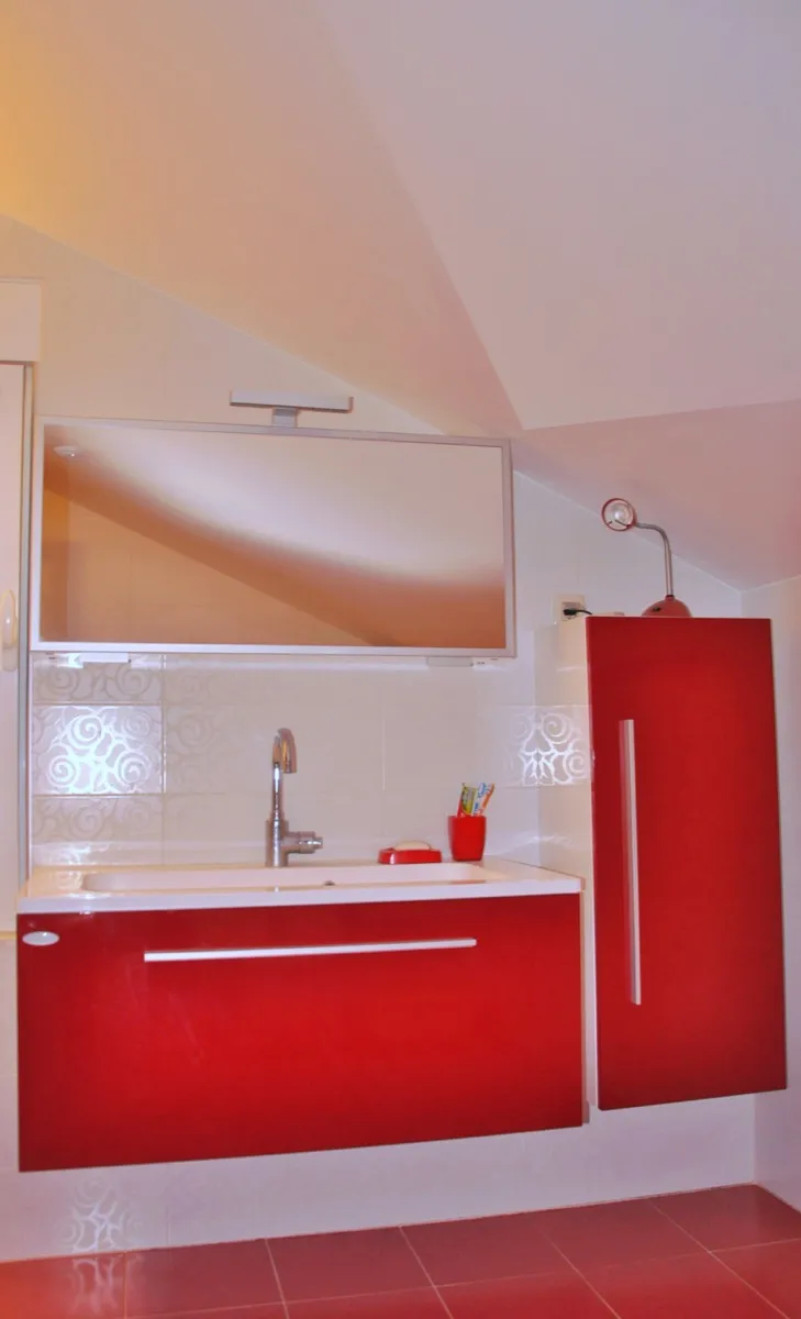 Red vanity with sink, mirror above, toothbrushes visible on counter against tiled wall.