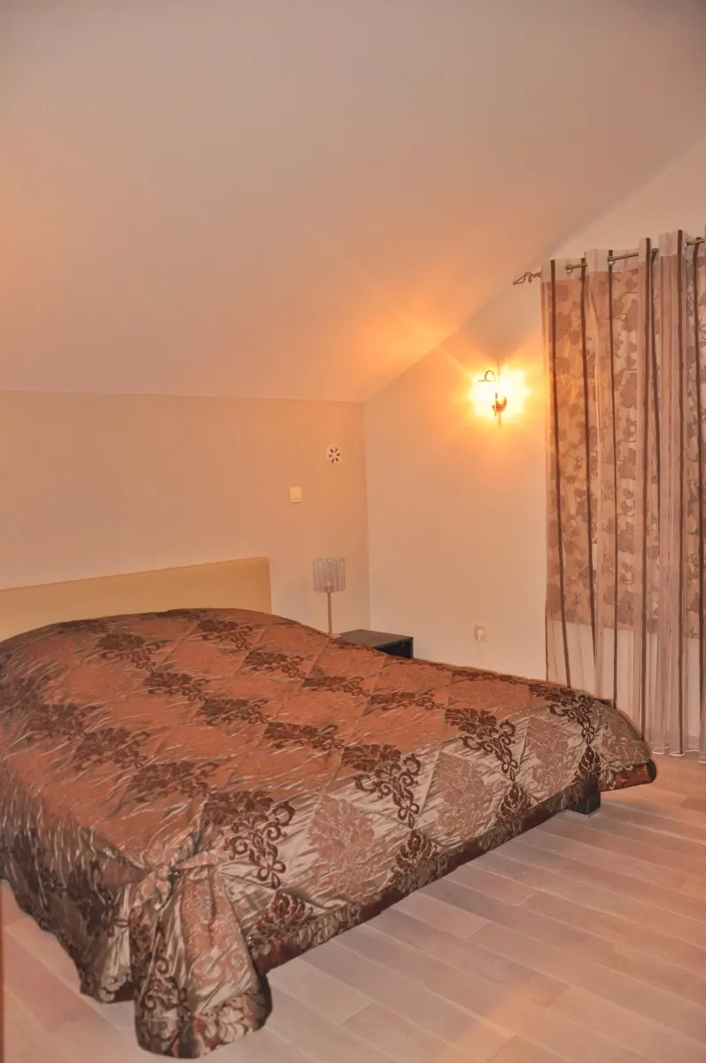 Bedroom featuring a double bed with brown patterned cover, wall sconce, floral curtains, and light wood flooring.