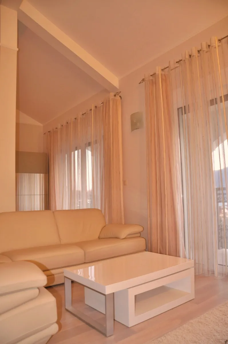 Bright room with a beige sofa, white coffee table, and long sheer curtains covering large windows.