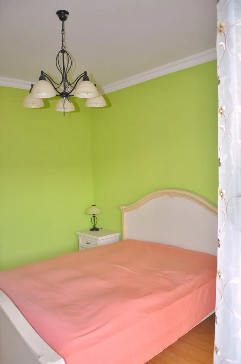 Bedroom featuring a bed with pink cover, white headboard, nightstand, and chandelier against bright green walls.