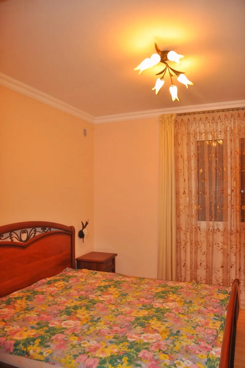 Bedroom featuring a wooden bed with floral bedding, a nightstand, sheer curtains, and a ceiling light fixture.