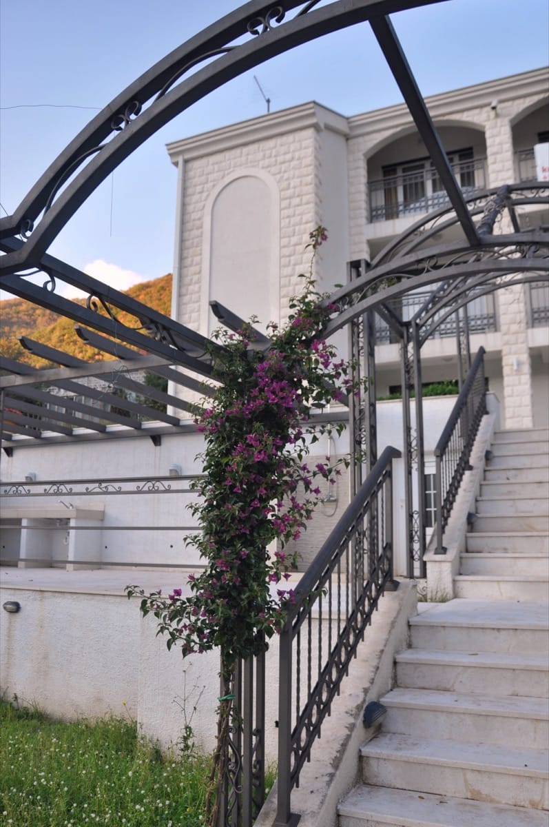 Villa in Đenovići, Montenegro: stone staircase, wrought-iron railings, pergola, and blooming bougainvillea on the house facade.