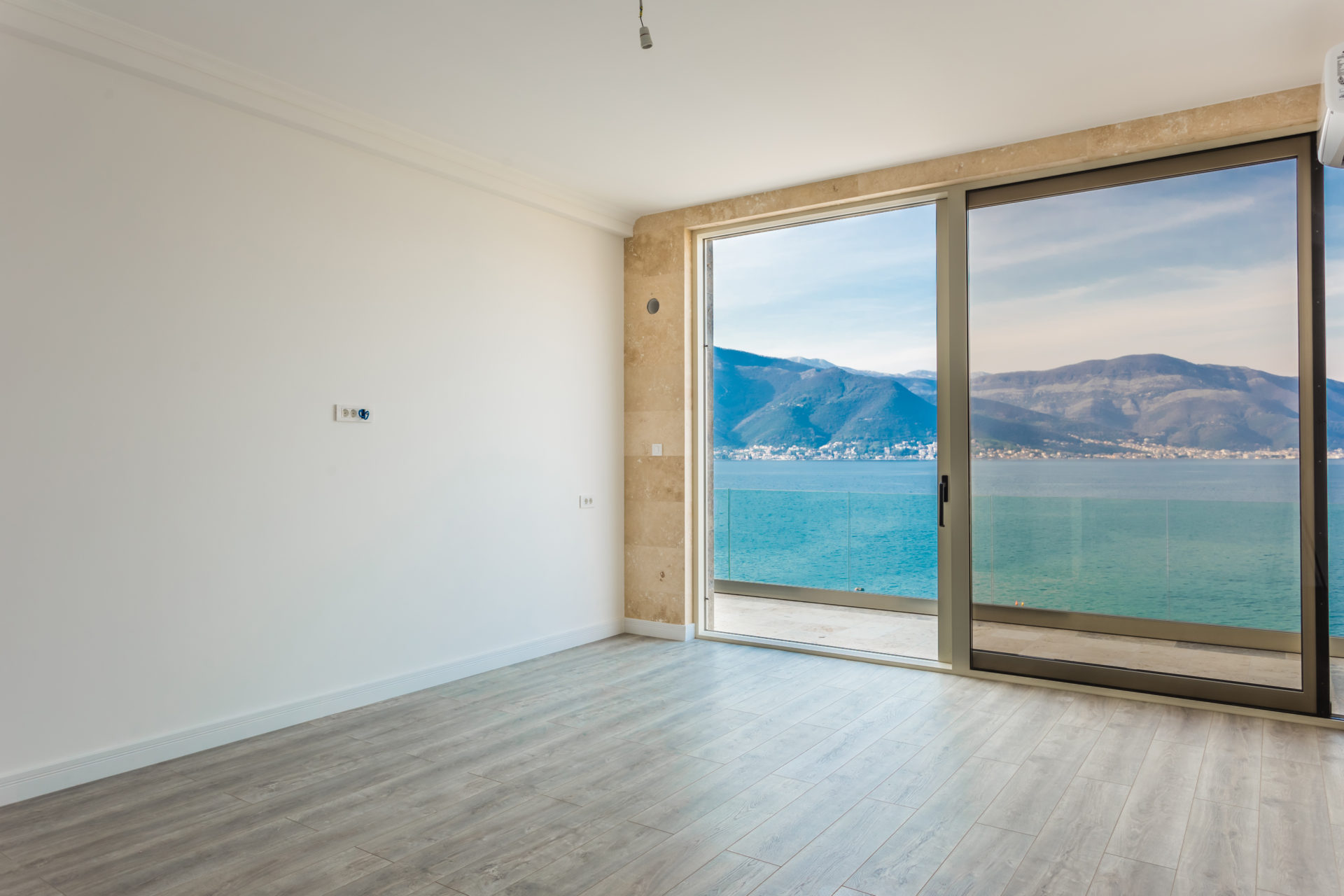 Bright living room with panoramic sea and mountain views in a villa, Krašići, Montenegro: stone finishes and access to the terrace.