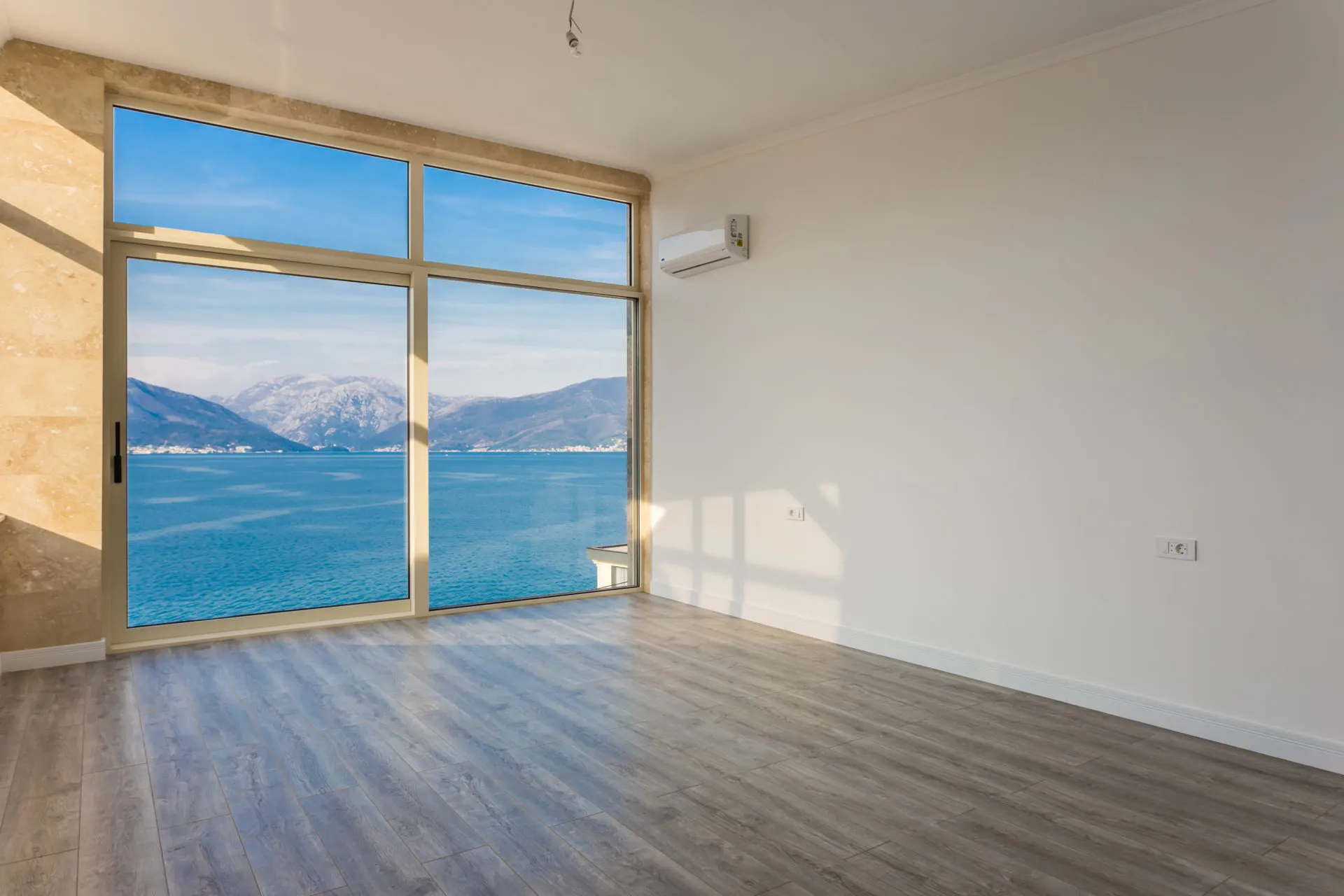 Empty room with grey laminate flooring and a large window overlooking the sea and mountains.