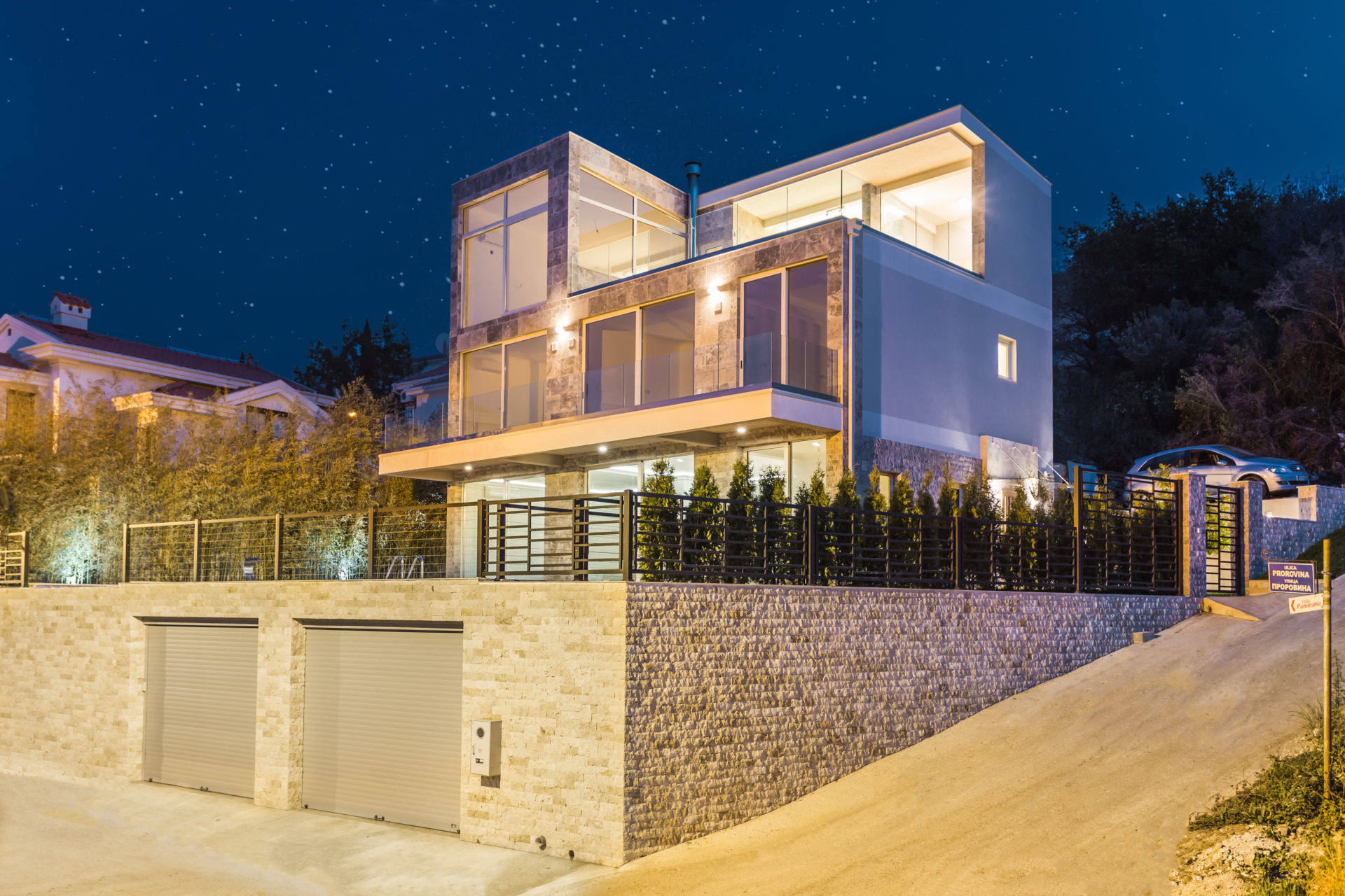 Modern three-story villa with panoramic windows and a garage in Krašići, Montenegro, front view at night.