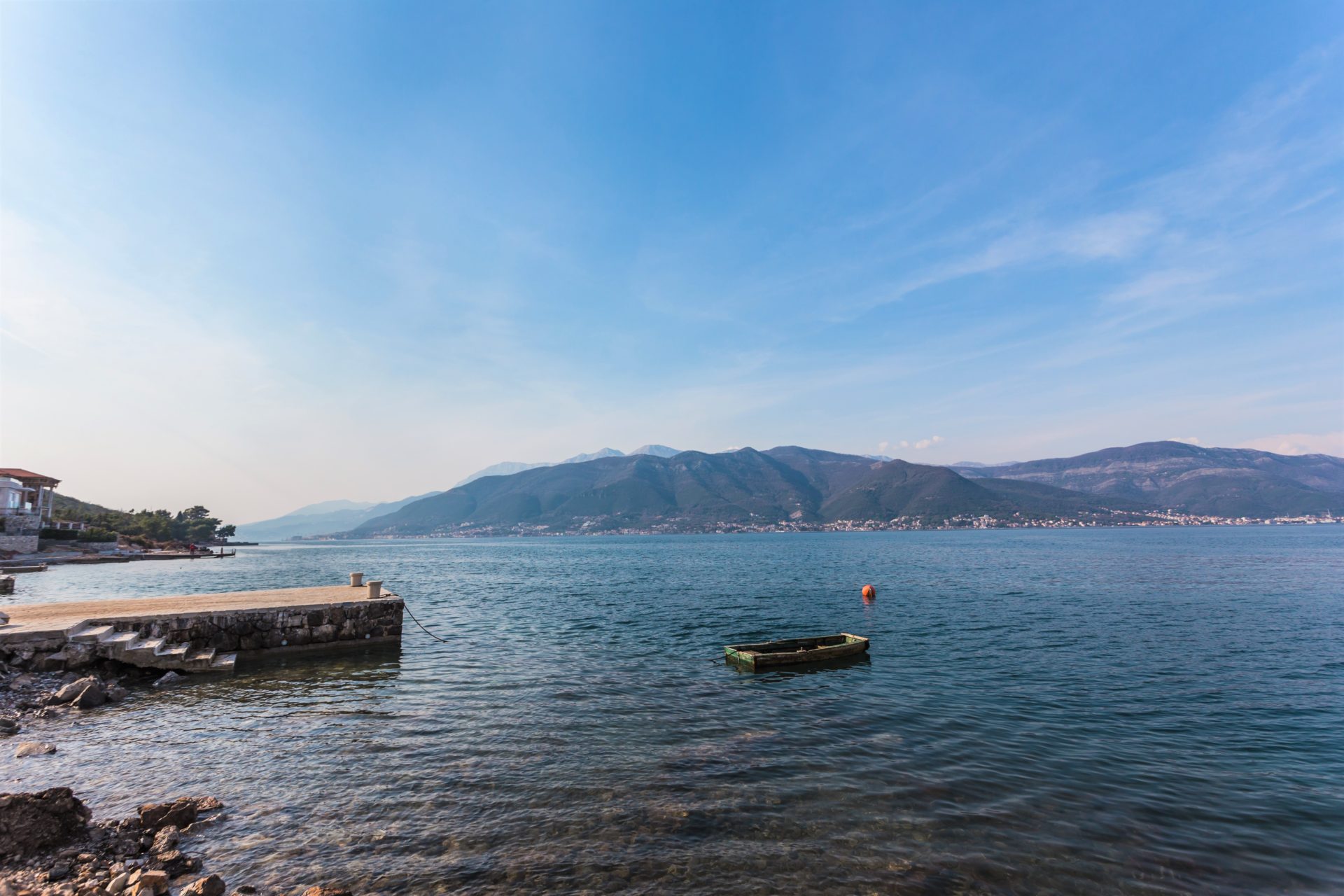 Sea and mountain view from a private pier by a villa in Krašići, Montenegro: a stone jetty and a boat in clear water.