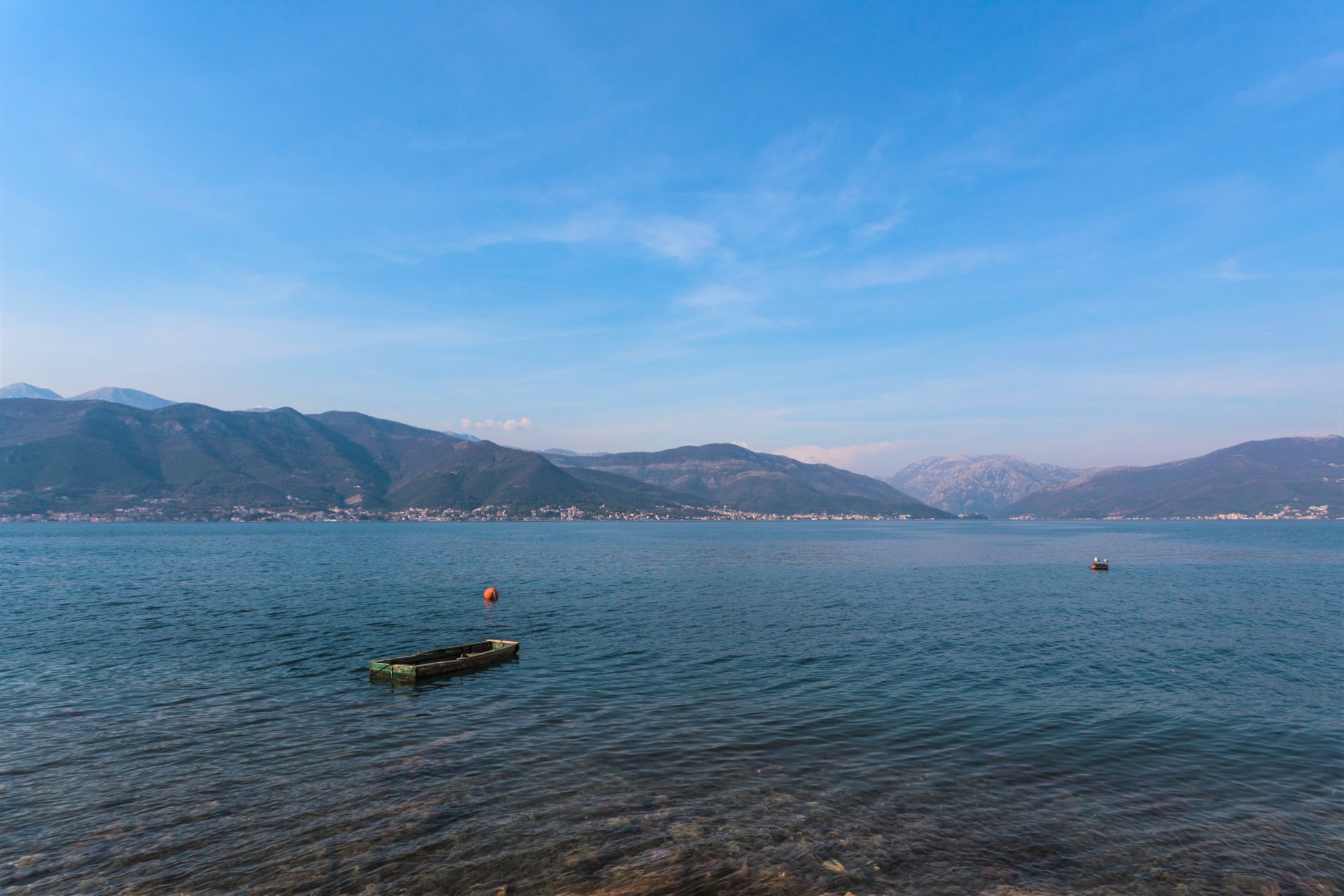 Panoramic view of the sea and mountains in Krašići, Montenegro: a boat by the shore and a picturesque villa landscape on the coast.