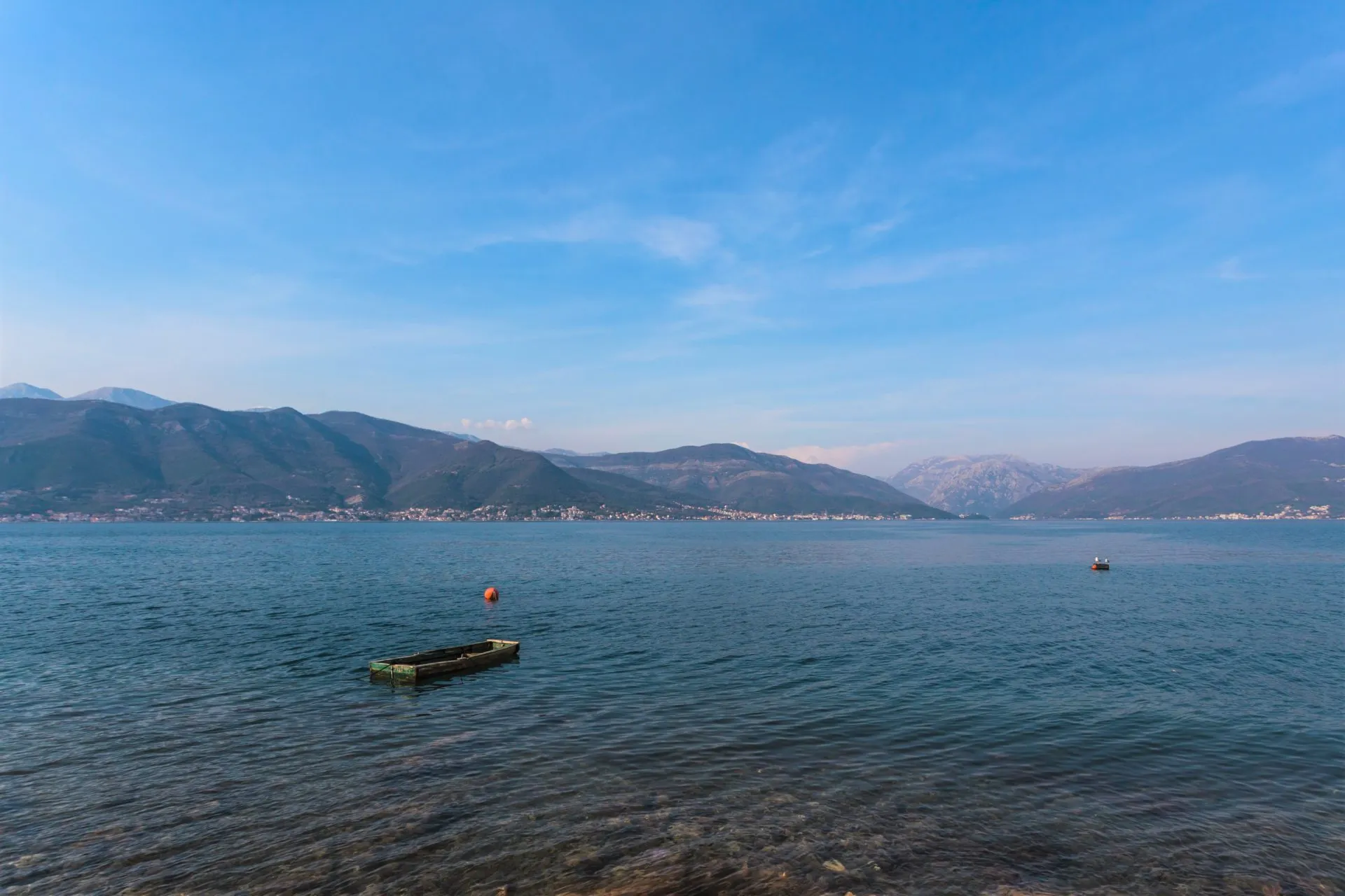 Scenic view of a large body of water with a small wooden boat and orange buoy against a backdrop of mountains.