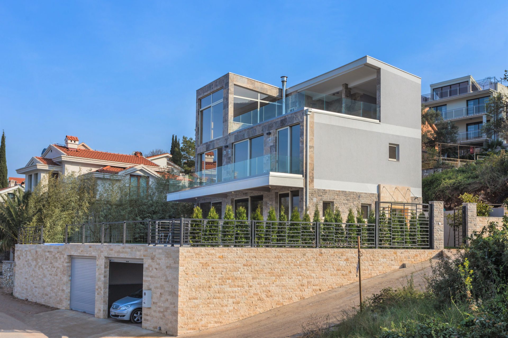 Modern three-story villa with panoramic windows and a garage in Krašići, Montenegro: view of the facade and terraces.
