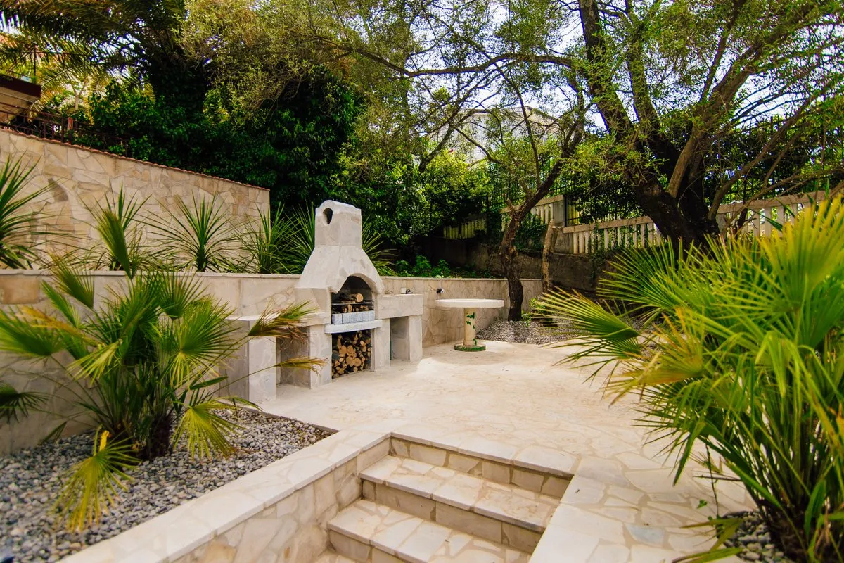 Outdoor stone courtyard featuring a built-in pizza oven, steps, and tropical plants.