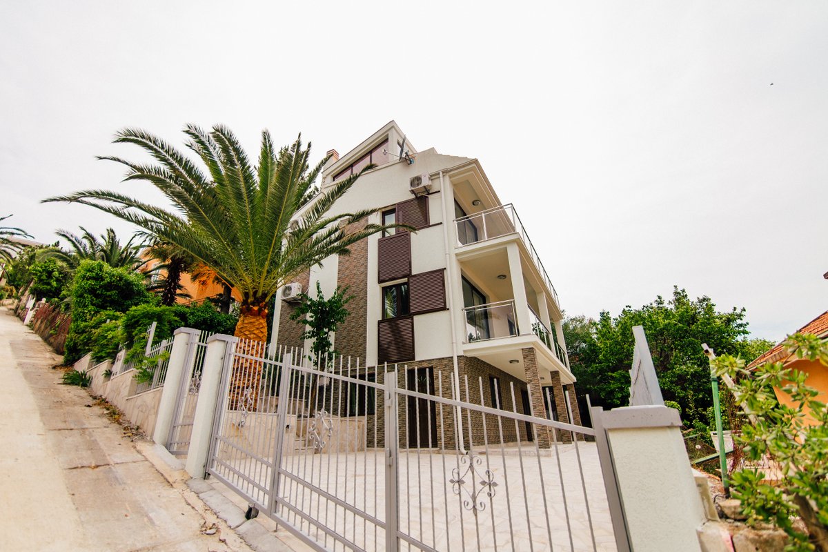 Modern three-story villa with terraces and a palm tree in the yard, Krašići, Montenegro. Facade with stone finish.