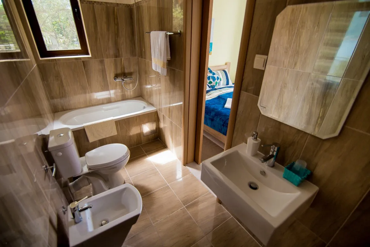 Bathroom featuring a bathtub, toilet, sink, and bidet. Walls and floor are covered in brown tiled material.