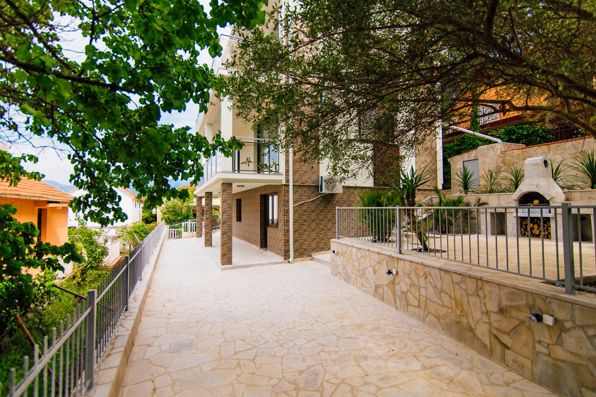 Modern villa in Krašići, Montenegro: terrace with stone finish, barbecue area, and view of the house facade.