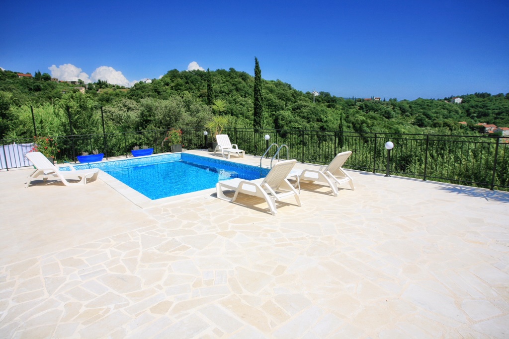 Open-air swimming pool with sun loungers on the terrace of a villa in Herceg Novi, Montenegro, with panoramic views of green hills.