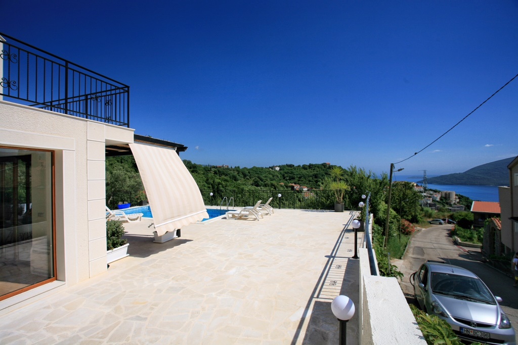 Terrace of a villa with a pool and sea view in Herceg Novi, Montenegro: sun loungers, awning, and stone paving.