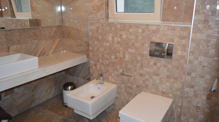 Bathroom with marble tiles, wall-mounted toilet, bidet, and vessel sink on a stone countertop.