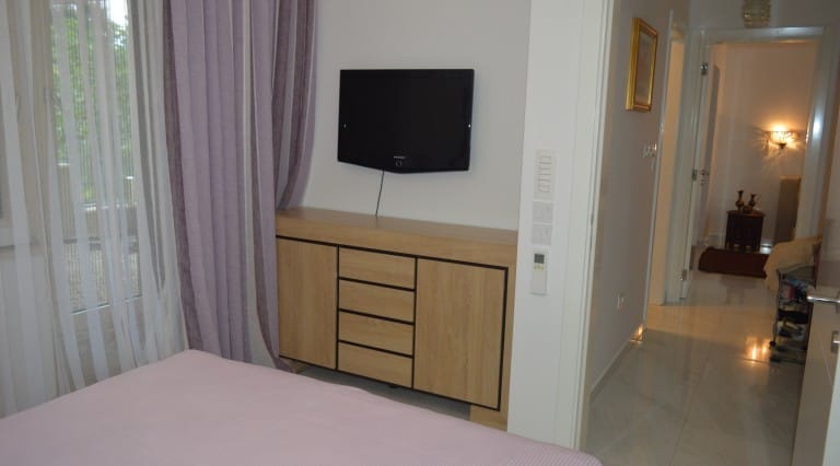 Bedroom interior with TV and dresser in an apartment, town of Ljuta, Montenegro: light finishes, view of the balcony and hallway.