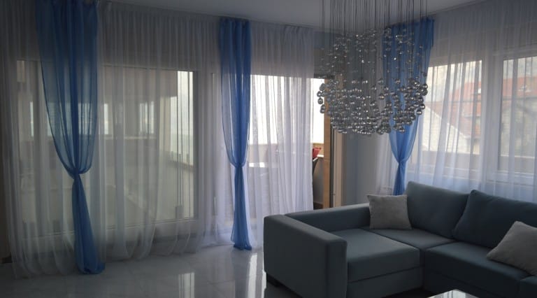 Living room in an apartment in Ljuta, Montenegro: blue sofa, panoramic windows with blue curtains, and a designer chandelier.